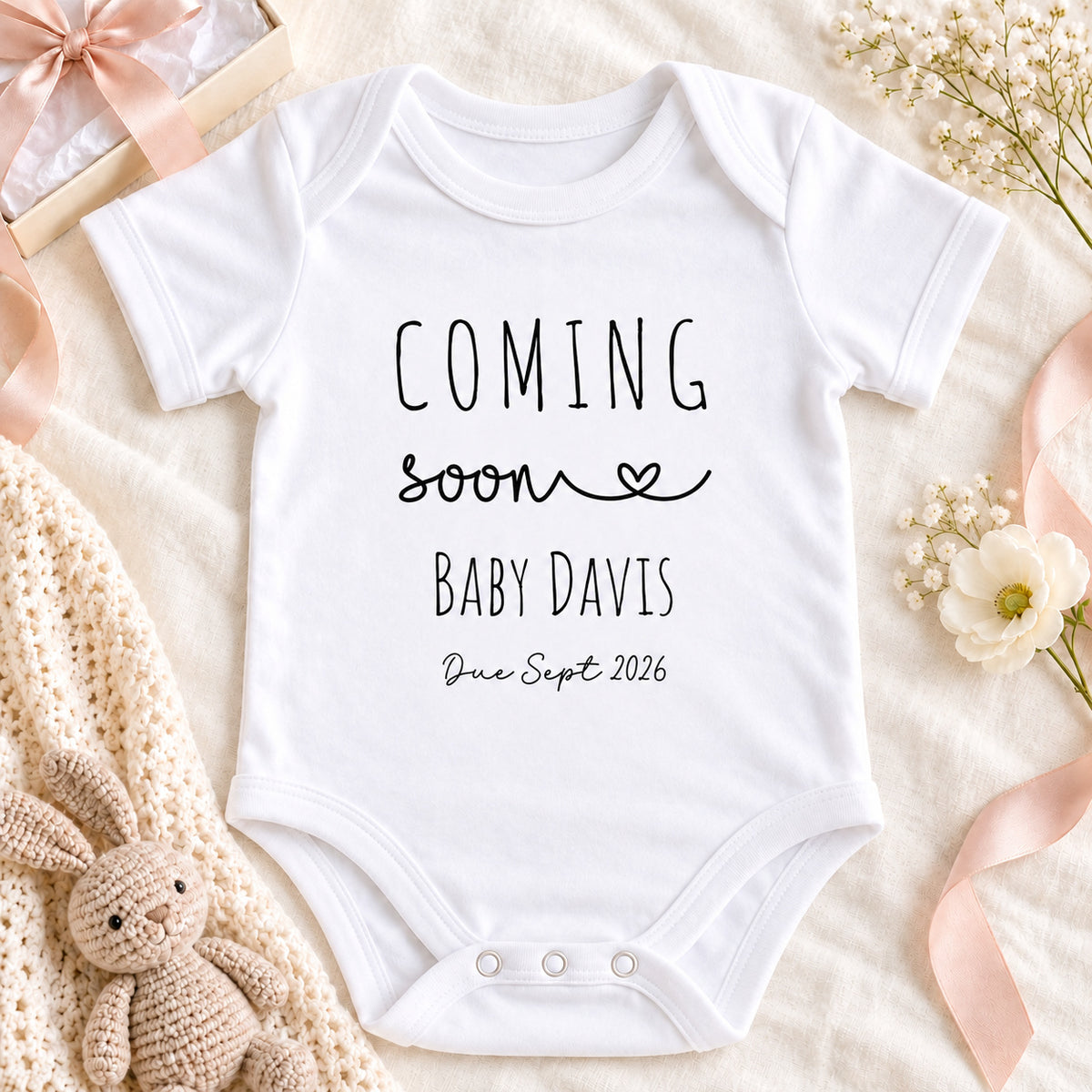 Square pregnancy announcement image of a white Coming Soon Baby Davis Vest with September 2026 due date, styled on beige linen beside a coffee cup, gift box and ribbon.