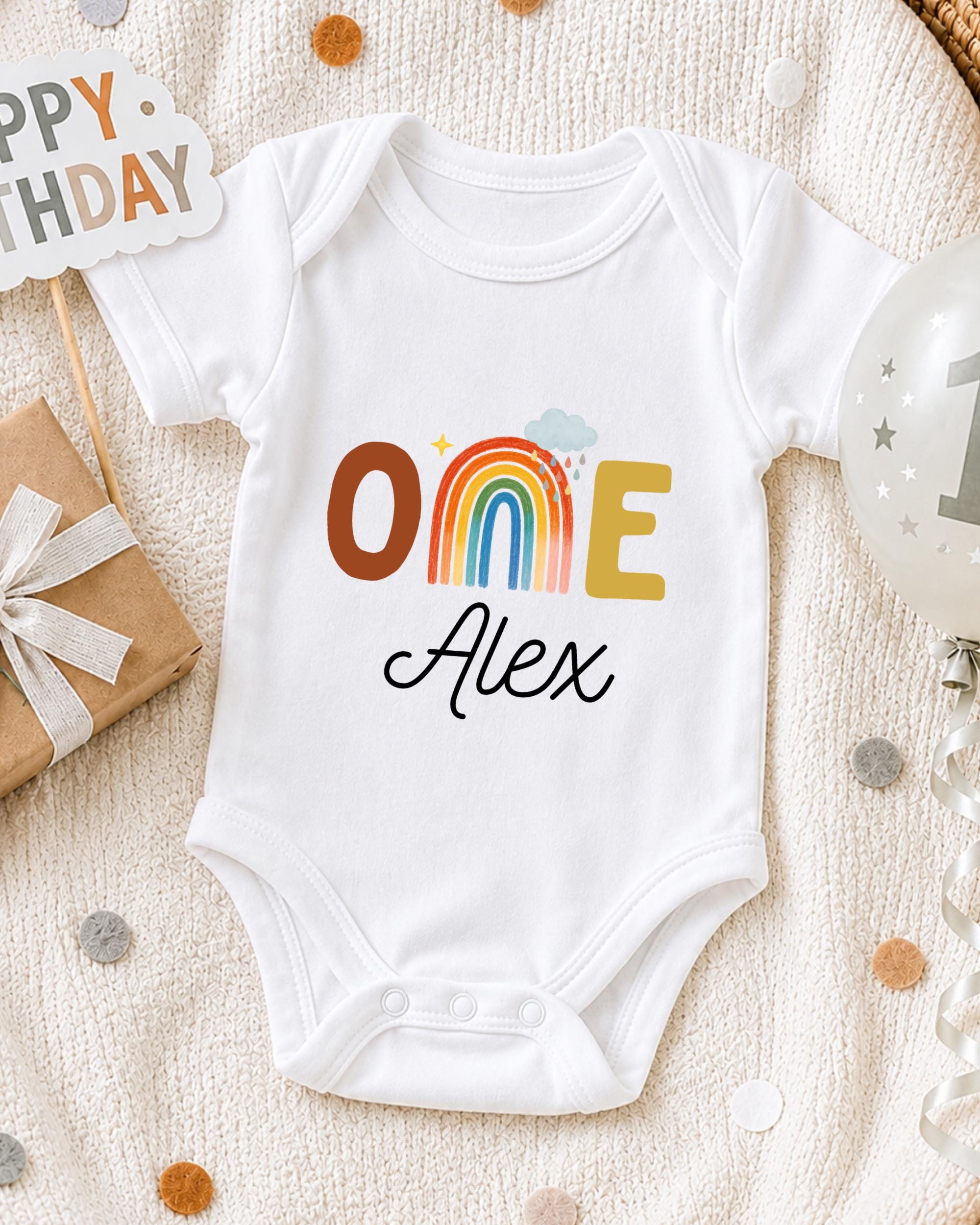 A white onesie with the text "ONE Alex" printed on it, surrounded by birthday decorations and a "Happy Birthday" sign.
