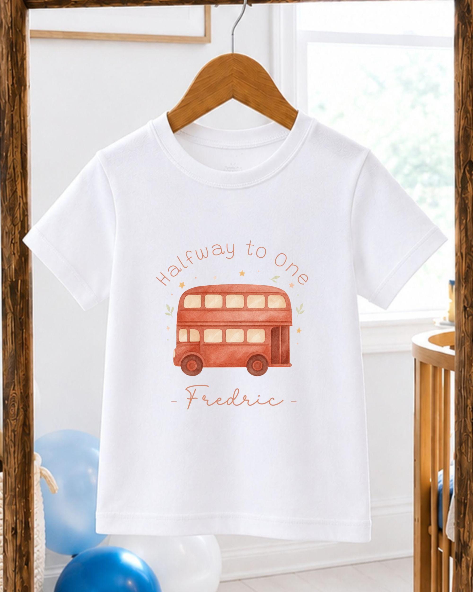 A white t-shirt with a printed image of a red double-decker bus and the text "Halfway to One - Frederic" printed on it.