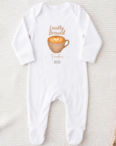 A white onesie with a graphic of a cup of coffee and the text "Locally Brewed Fredricine 2026" printed on it.