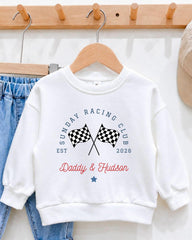 A white sweatshirt with a graphic design featuring a checkered flag and the text "Sunday Racing Club Est. Daddy & Hudson" printed on it.