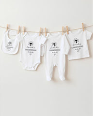 A row of white christening outfits hanging on a clothesline, each with a black cross and text indicating the christening date.