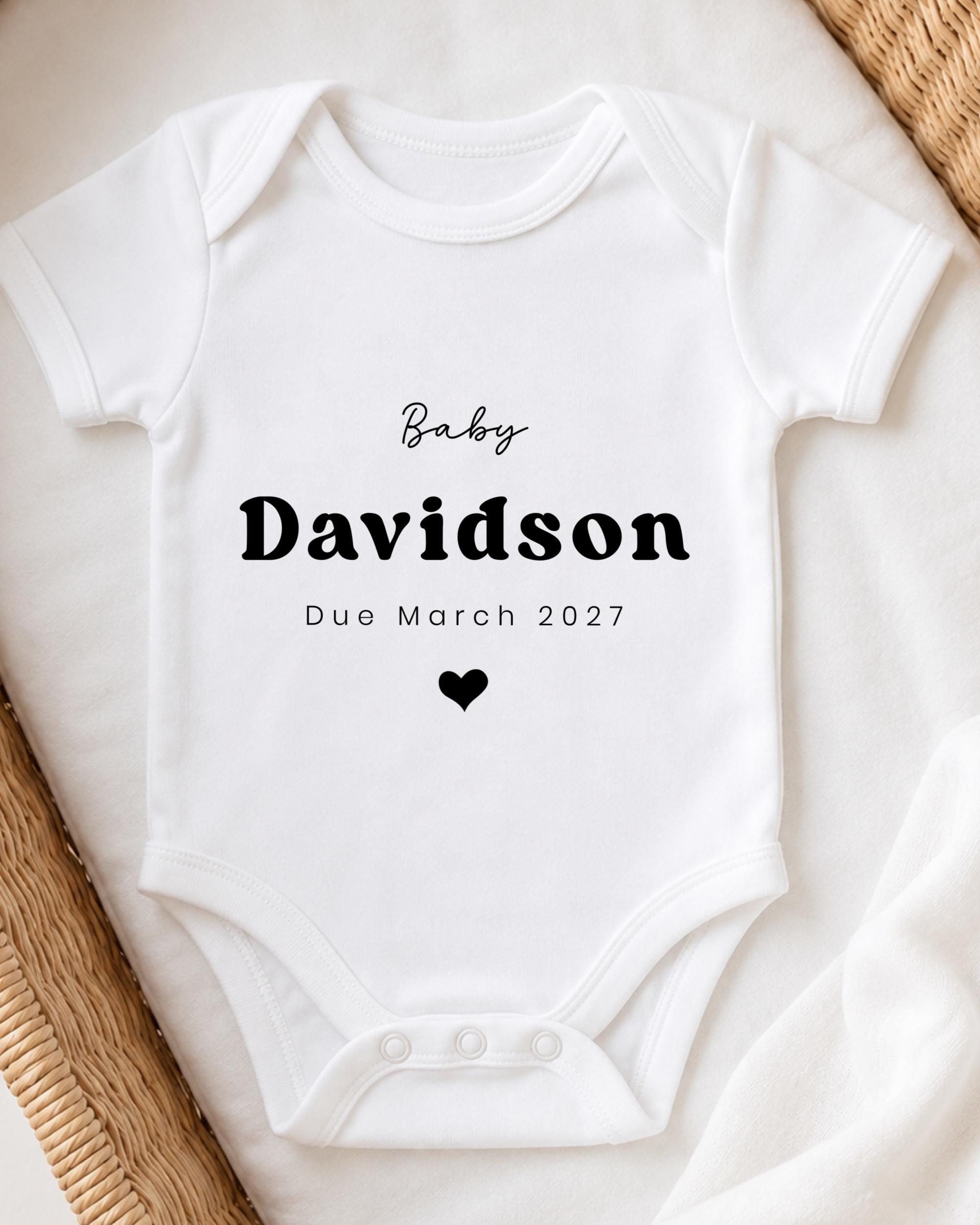A white baby onesie with the text "Baby Davidson Due March 2027" printed on it.