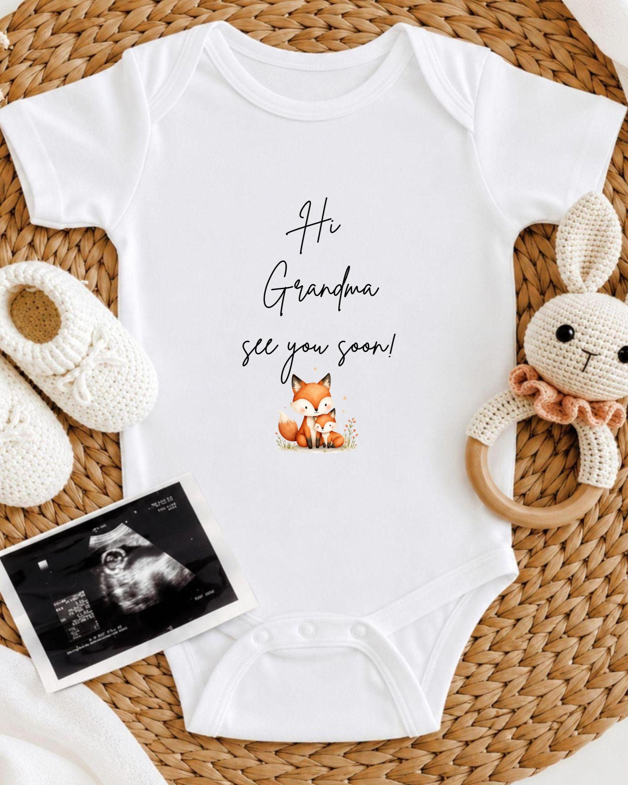 A baby onesie with the text "Hi Grandma see you soon!" printed on it, along with a crocheted bunny toy and a black and white baby photo.