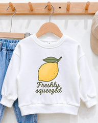 A white sweatshirt with a yellow lemon graphic and the text "Freshly squeezed" printed on it, hanging on a wooden hanger.