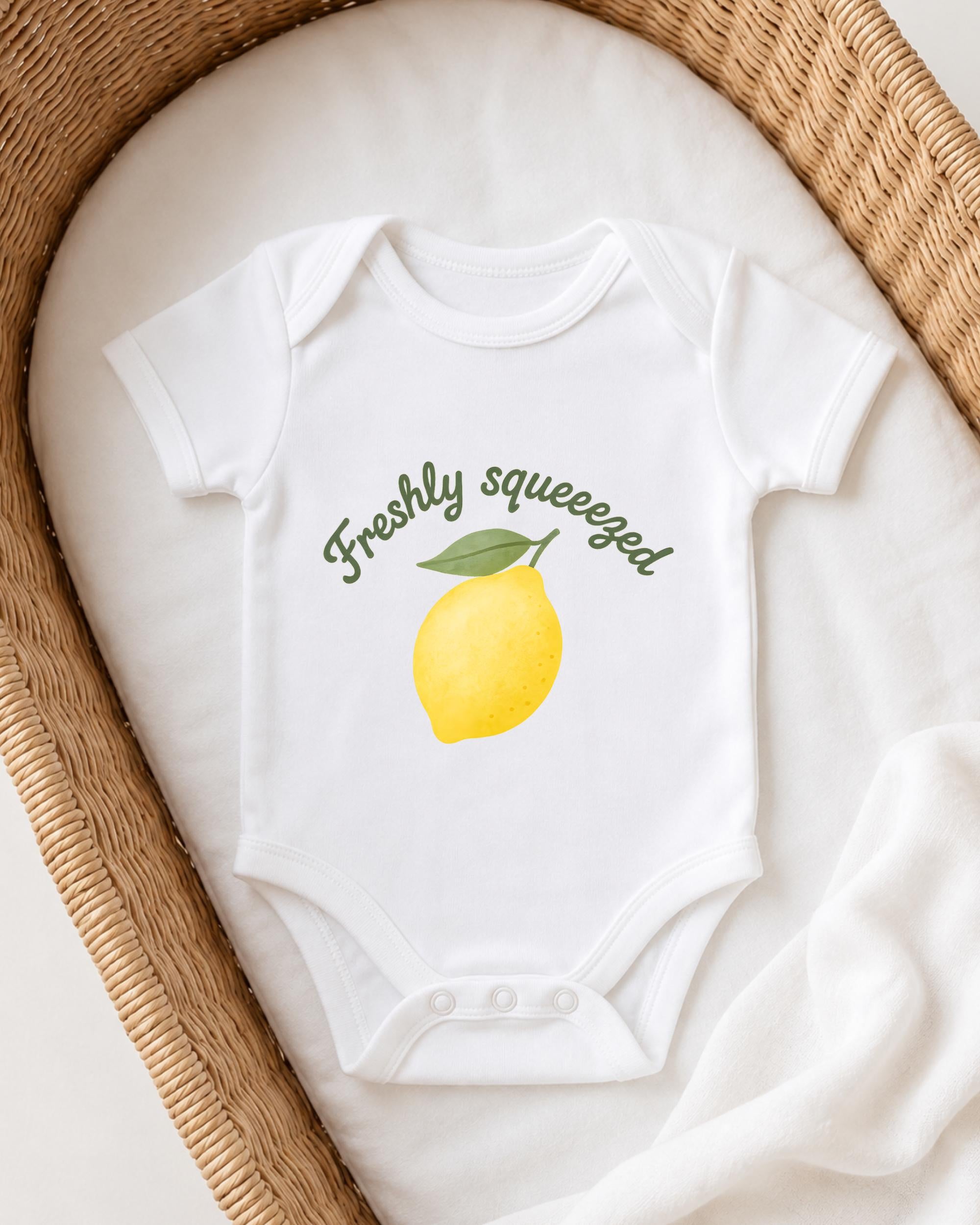 A white onesie with a lemon graphic and the text "Freshly squeezed" printed on it, placed in a woven basket.