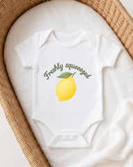 A white onesie with a lemon graphic and the text "Freshly squeezed" printed on it, placed in a woven basket.