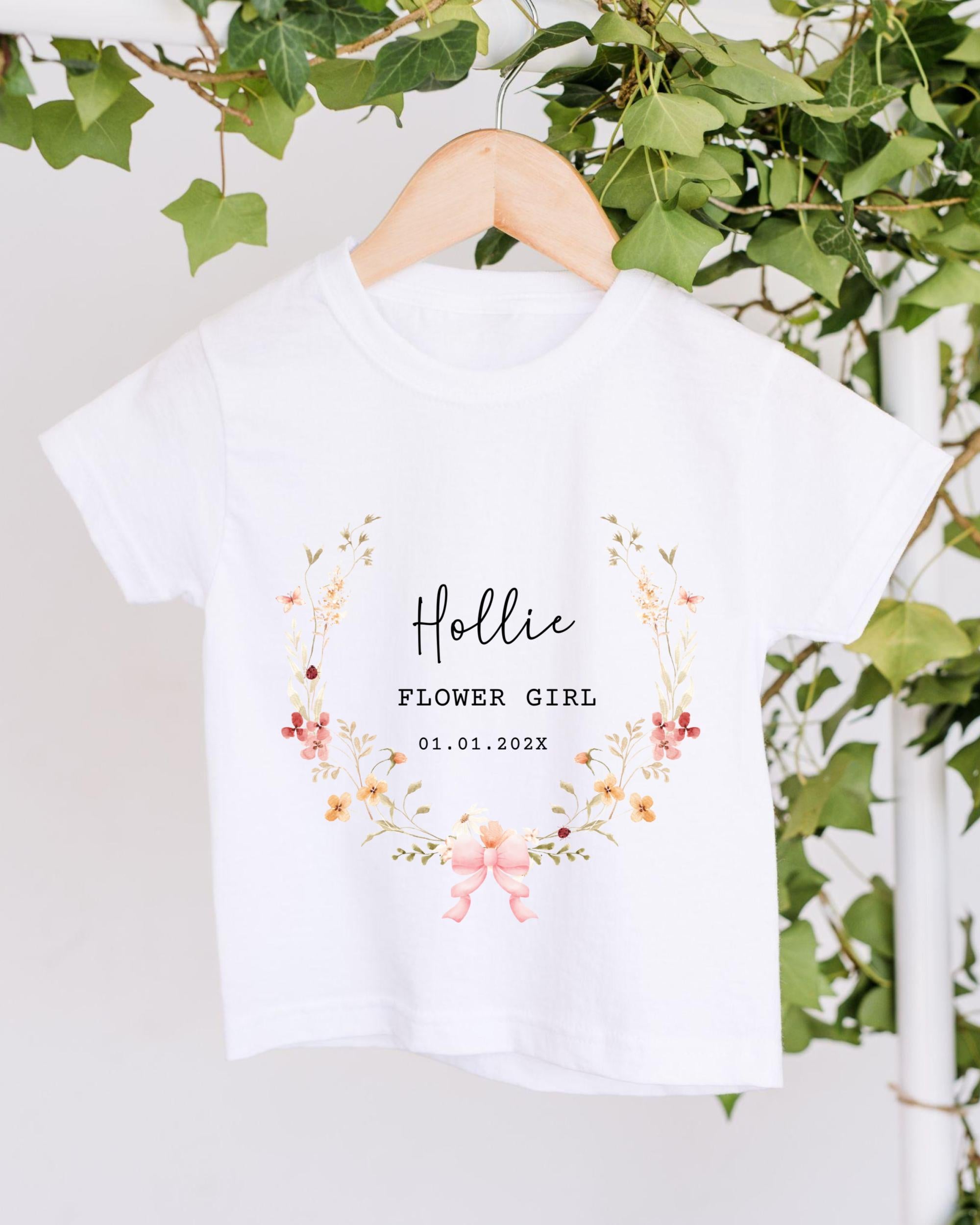 A white t-shirt with a floral design and text printed on it, hanging on a wooden hanger.