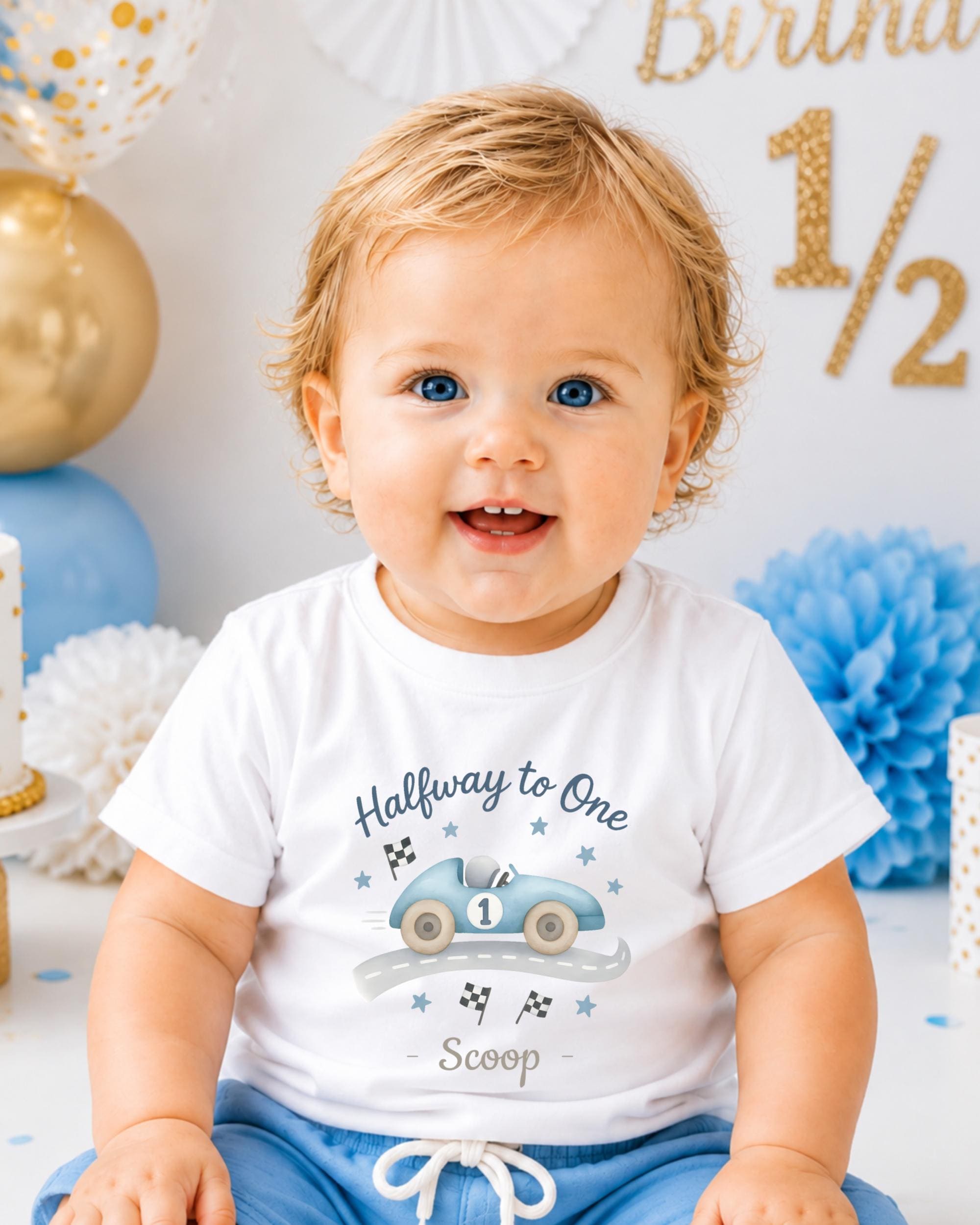 A smiling baby boy wearing a white t-shirt with a graphic of a race car and the text "Halfway to One Scoop" is sitting in front of a birthday party backdrop.