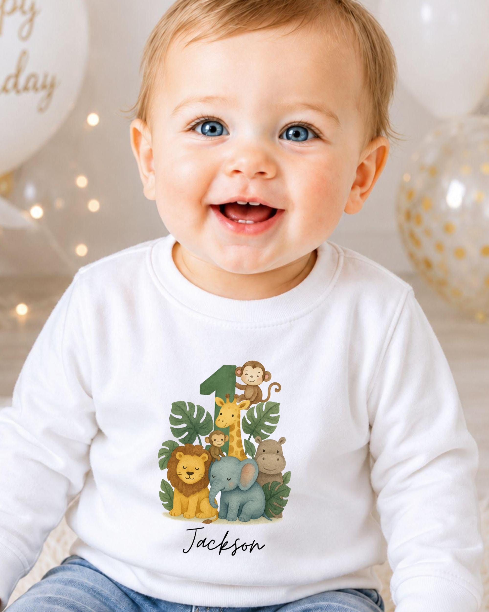 A smiling baby boy wearing a white long-sleeved shirt with a cartoon illustration of various animals, including a lion, giraffe, and elephant, along with the name "Jackson" printed on it.