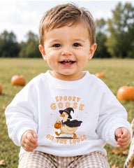 A smiling baby boy wearing a white sweatshirt with a cartoon goose and the text "Spooky GOOSE ON THE LOOSE" printed on it.