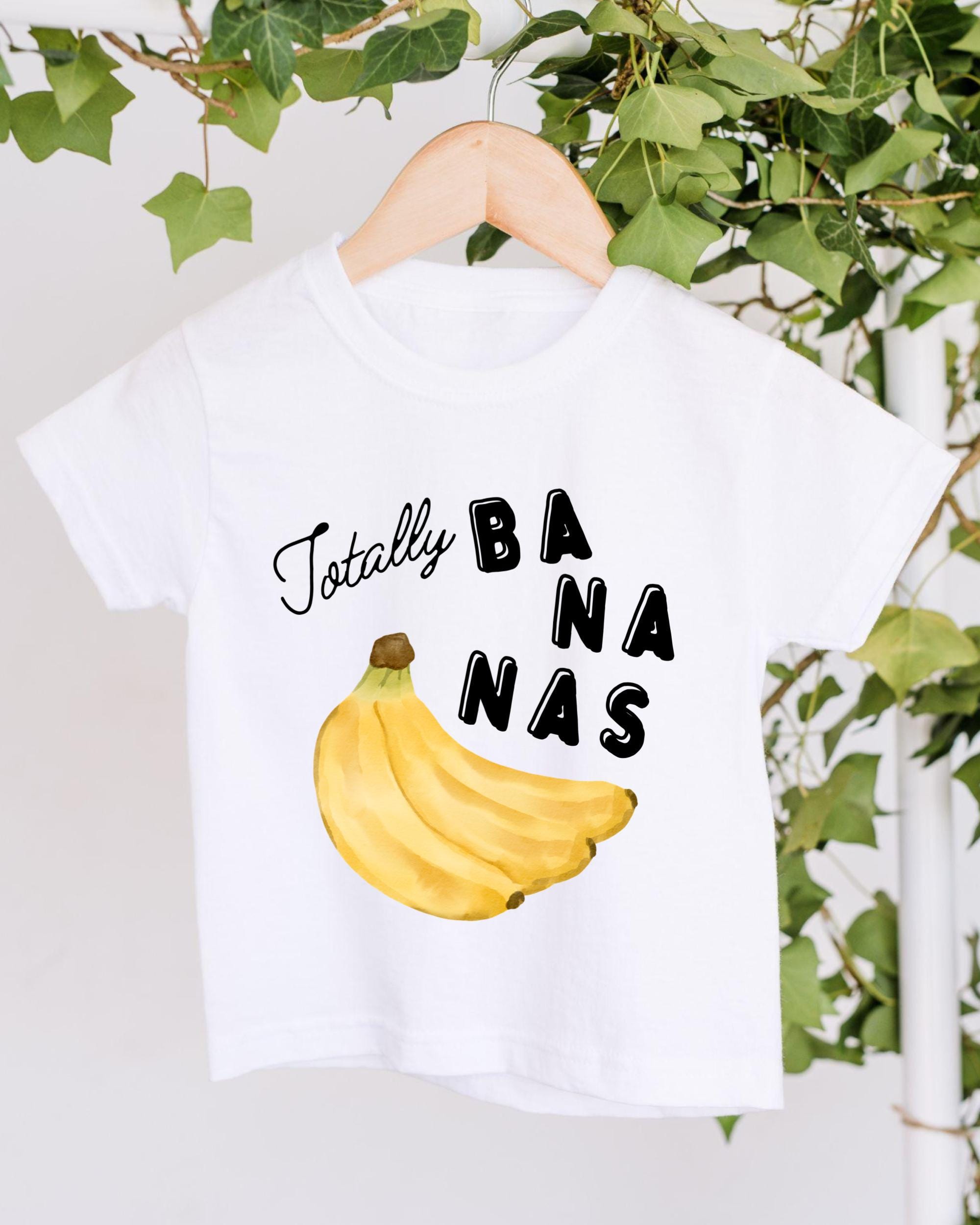 A white t-shirt with a graphic of a banana and the text "Totally BANANA" printed on it, hanging on a wooden hanger.