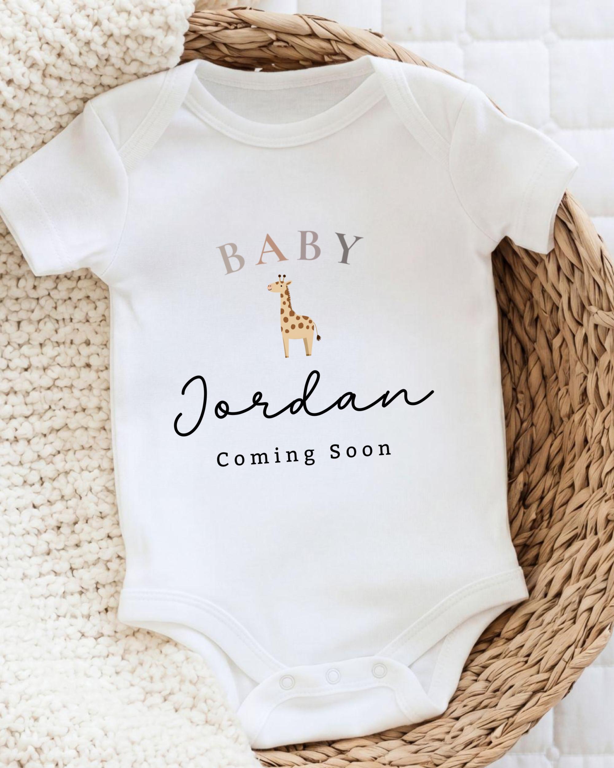 A white baby onesie with the text "BABY Jordan Coming Soon" printed on it, along with a small giraffe illustration.