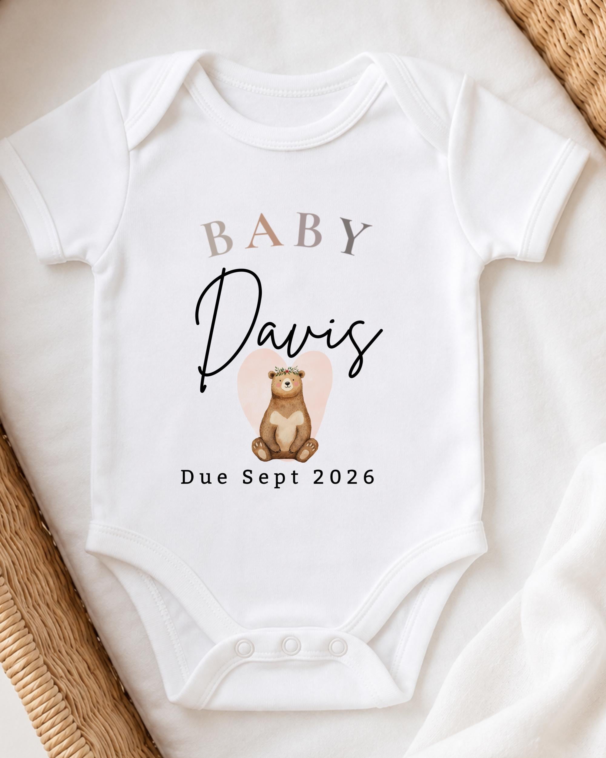 A white baby onesie with the text "BABY Davis Due September 2026" printed on it, along with an illustration of a bear.