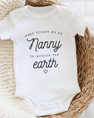 A white baby onesie with the text "Hand picked by my Nanny in heaven for earth" printed on it.