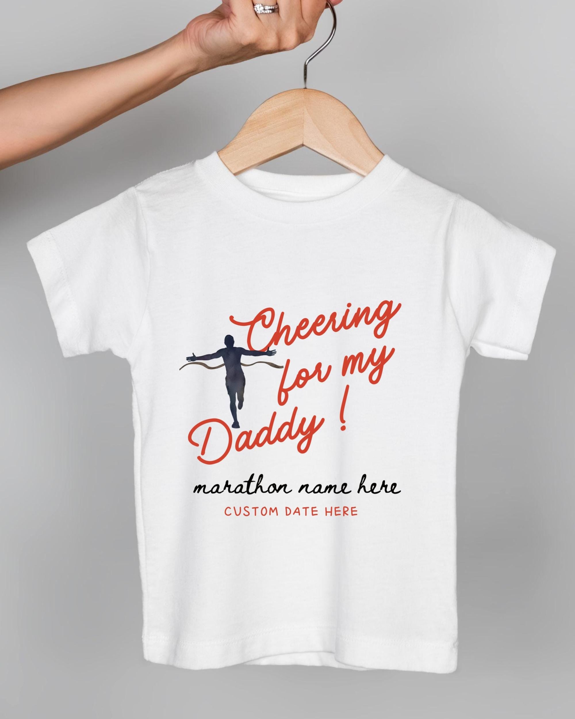 A white t-shirt with a graphic design featuring a person running and the text "Cheering for my Daddy!" printed on it.
