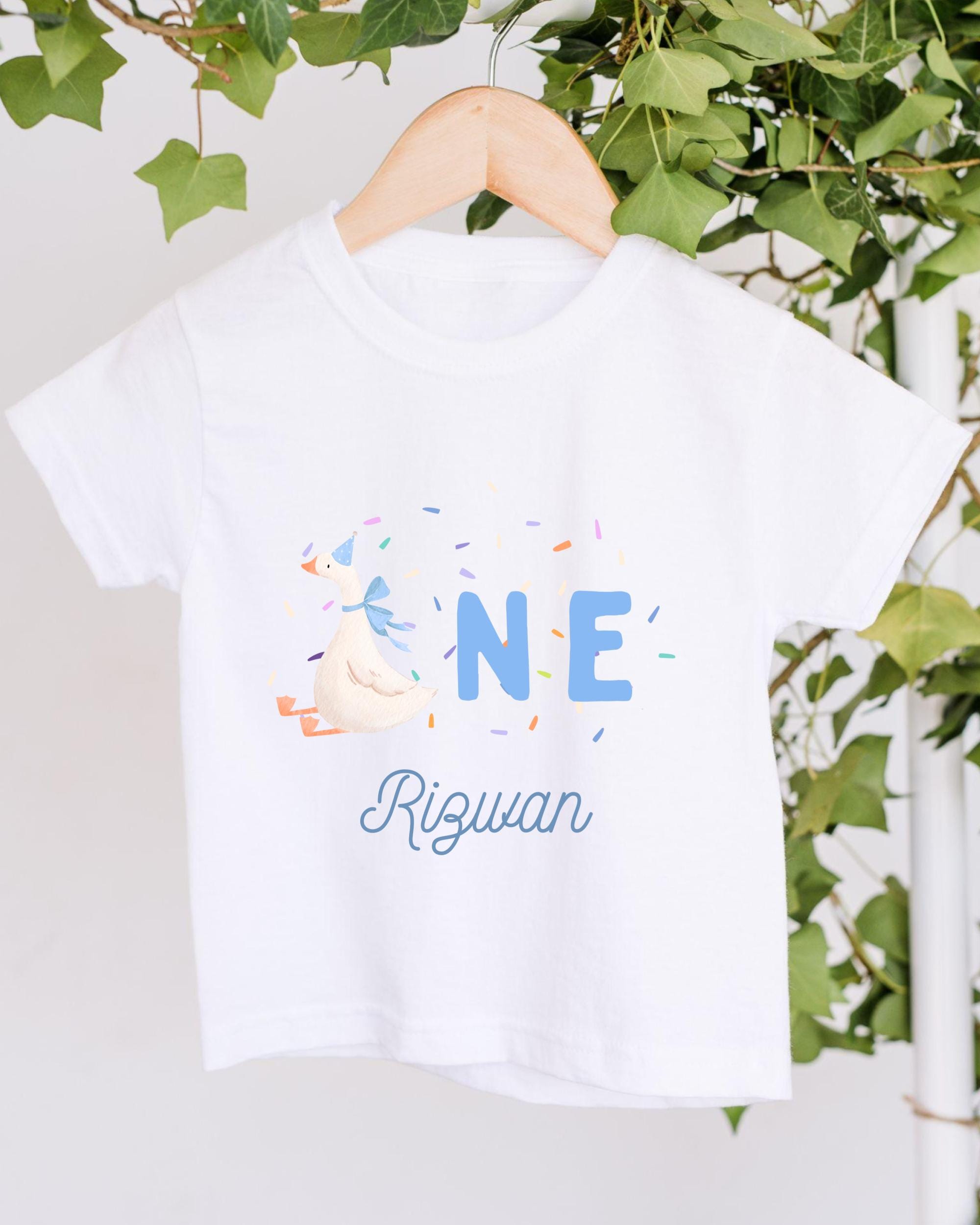A white t-shirt with a personalized text and graphic design hanging on a wooden hanger.
