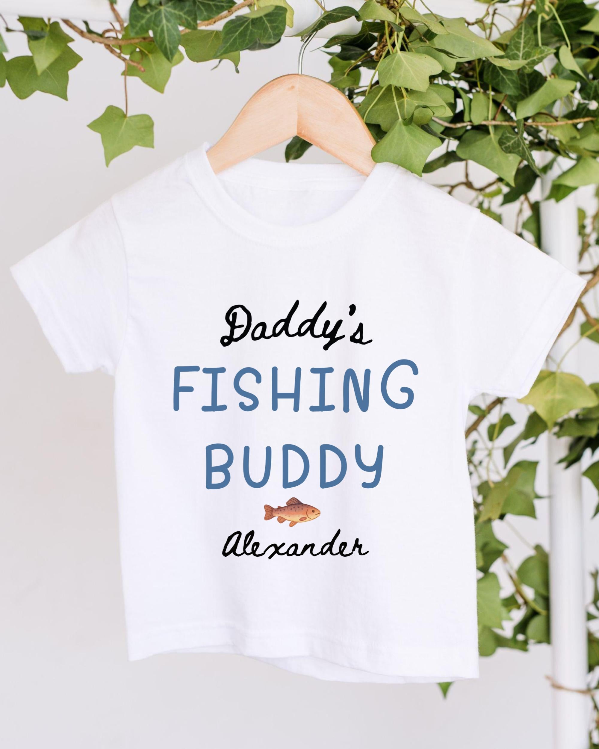 A white t-shirt with the text "Daddy's FISHING BUDDY Alexander" printed on it, along with a small fish graphic.