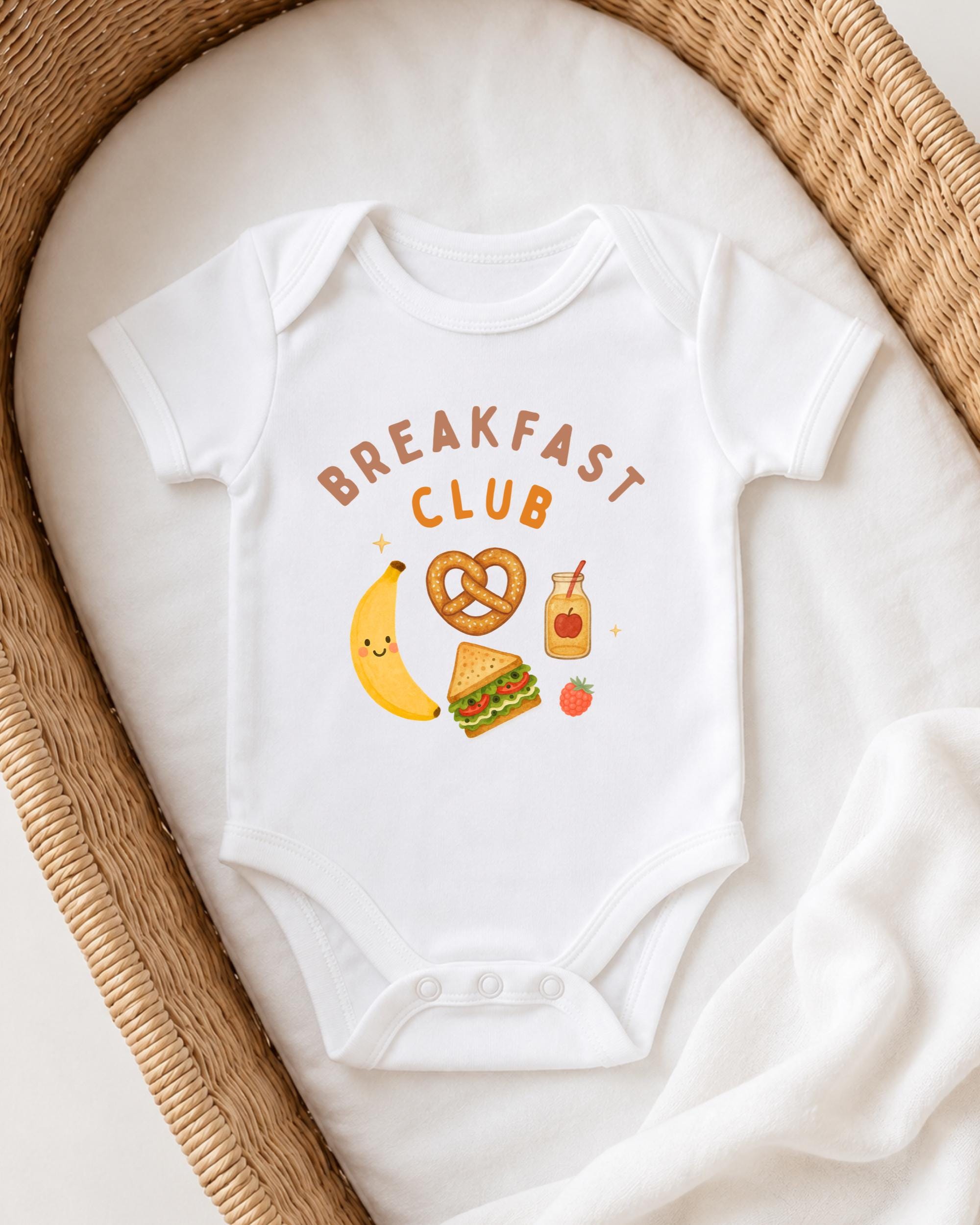 A white onesie with the text "BREAKFAST CLUB" printed on it, along with various breakfast-related icons such as a banana, pretzel, apple, and a jar of jam.