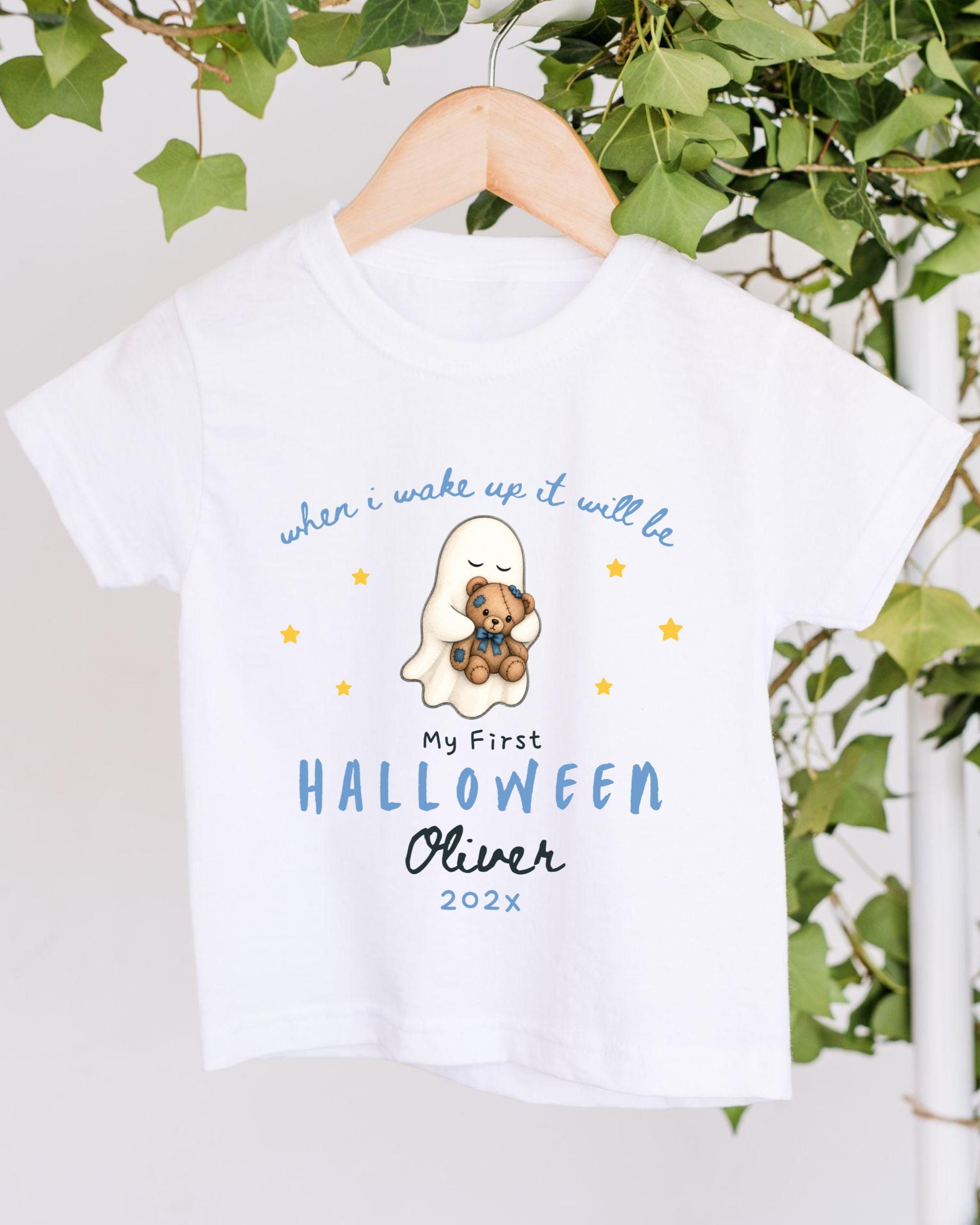A white t-shirt with a graphic design featuring a ghost and a teddy bear, along with text that says "when I wake up it will be My First Halloween Oliver 2023".