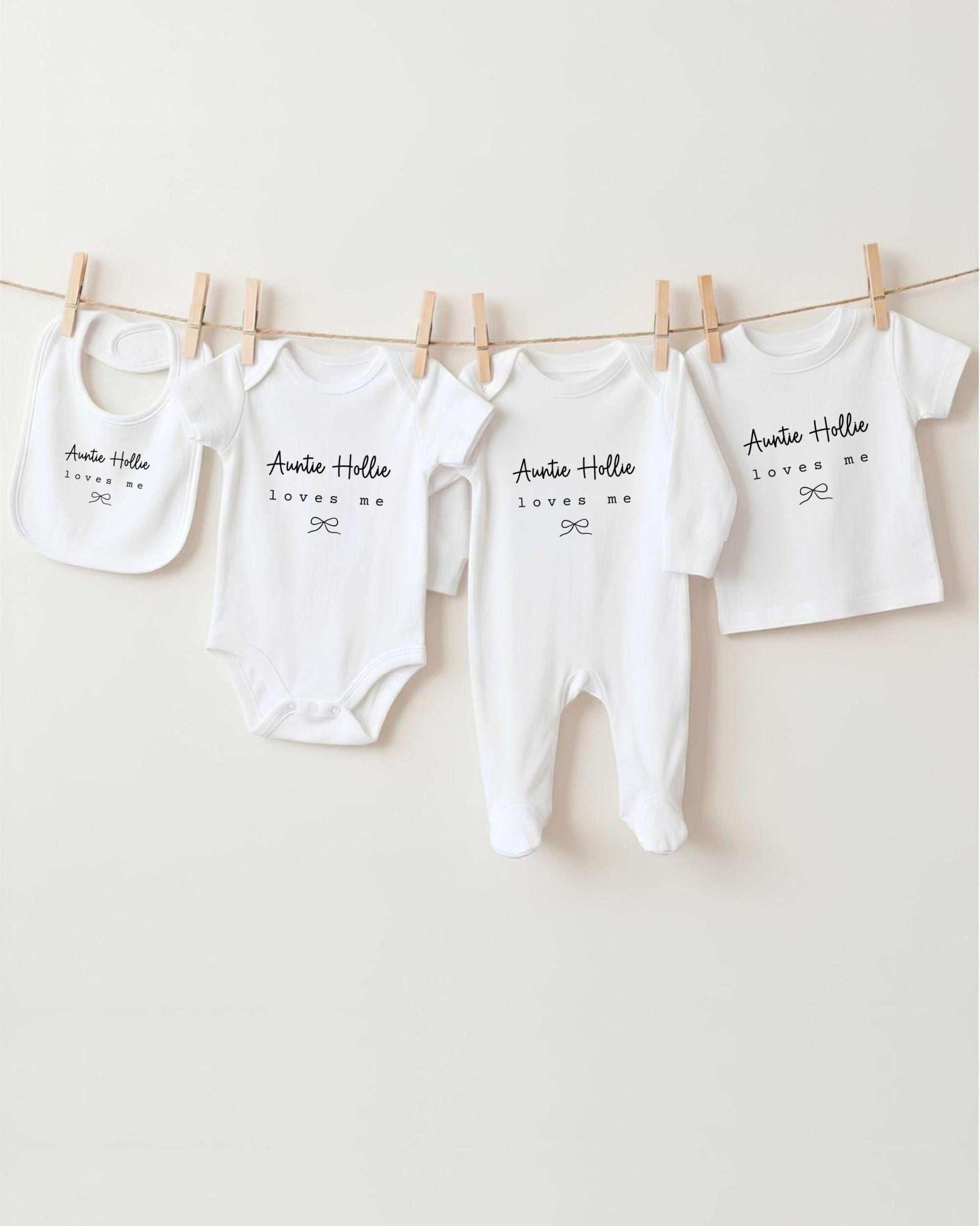 A row of four white baby clothes, including onesies and pajamas, hanging on a clothesline.