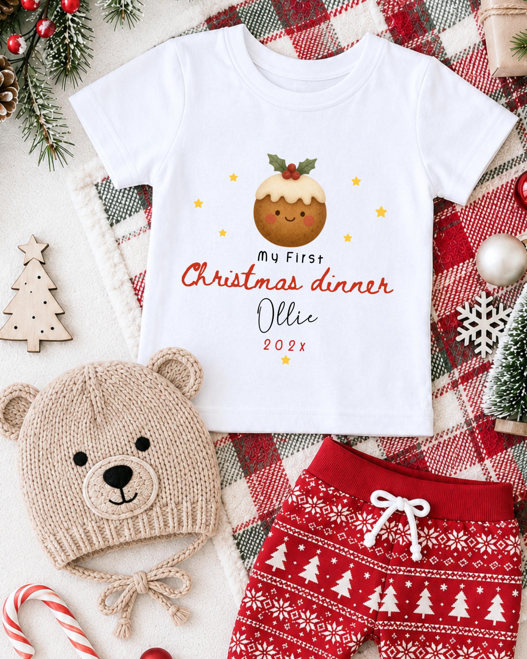 A white t-shirt with a Christmas-themed design, a beige knit hat with a Christmas tree design, and red and white patterned shorts, all arranged on a red and white plaid blanket.