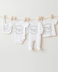 A row of four white baby clothes with black wing designs hanging on a clothesline.