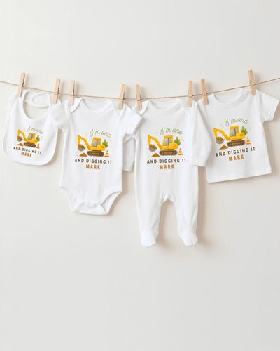 A collection of baby clothes, including bodysuits and pants, with a construction vehicle design printed on them.