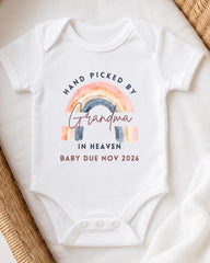 A white onesie with a rainbow graphic and text that reads "Hand picked by Grandma in Heaven Baby due Nov 2026".