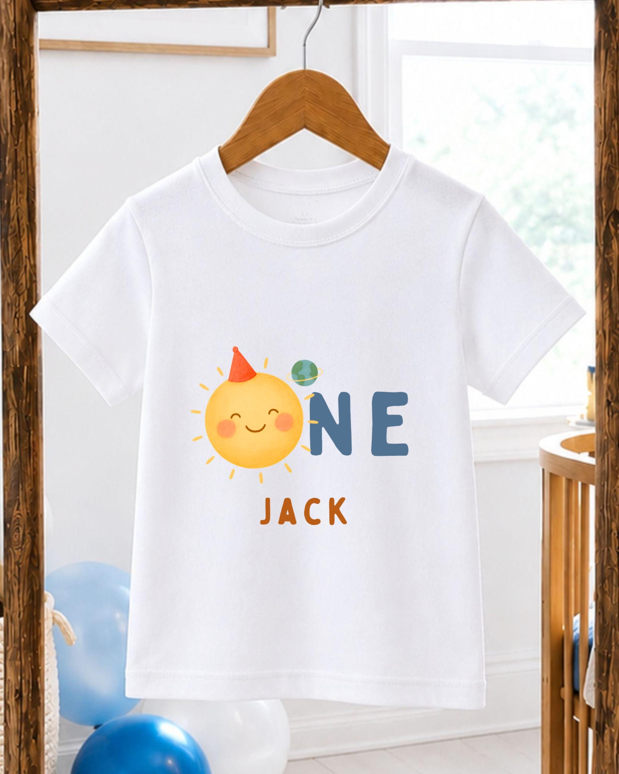 A white t-shirt with a cartoon sun and the text "ONE JACK" printed on it, hanging on a wooden hanger.