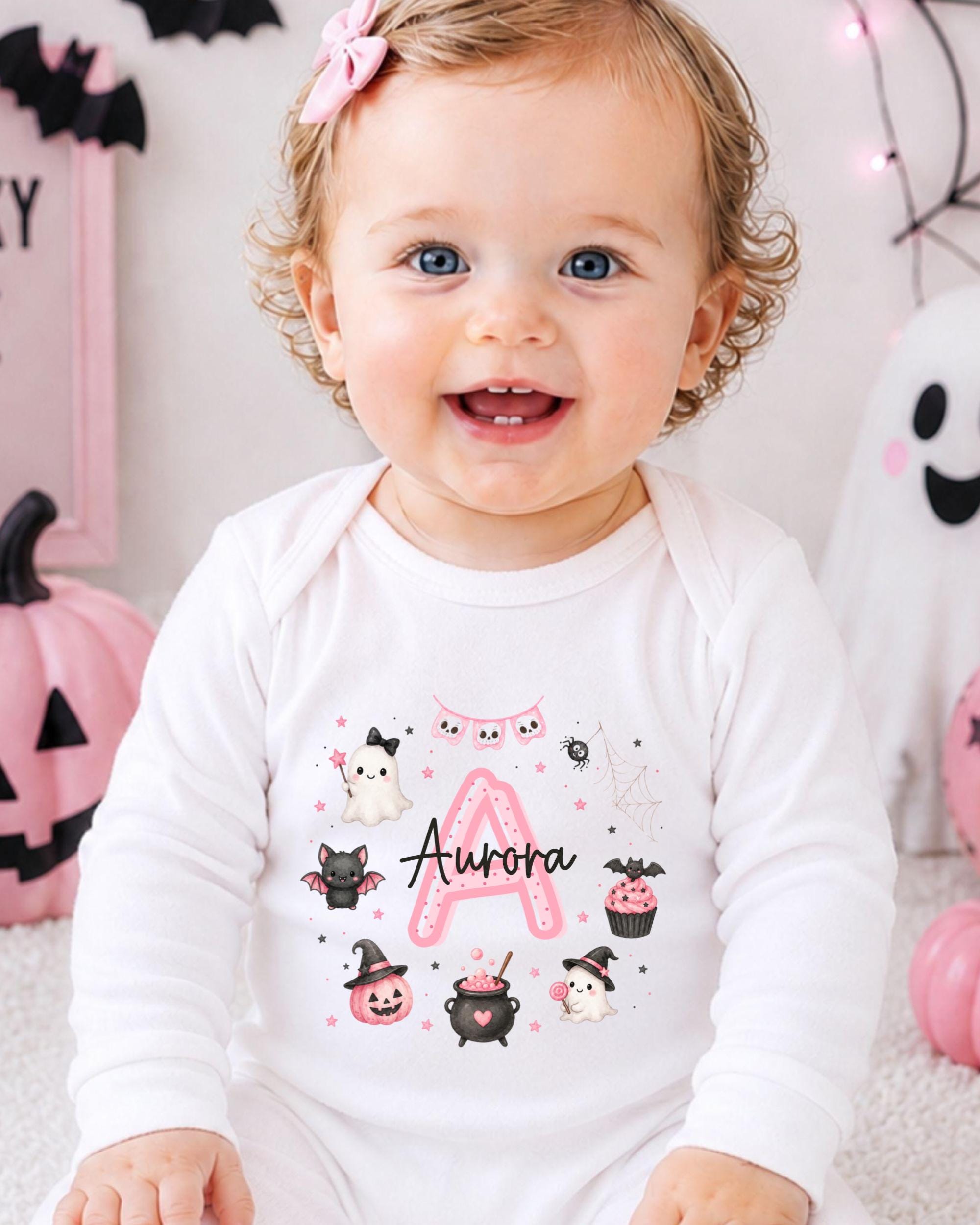 A smiling baby girl wearing a white onesie with a personalized name and Halloween-themed illustrations.