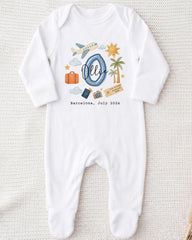 A white onesie with a graphic design depicting various travel-related items such as a suitcase, airplane, palm tree, and a sun. The text "Barcelona, July 2020" is also printed on the onesie.