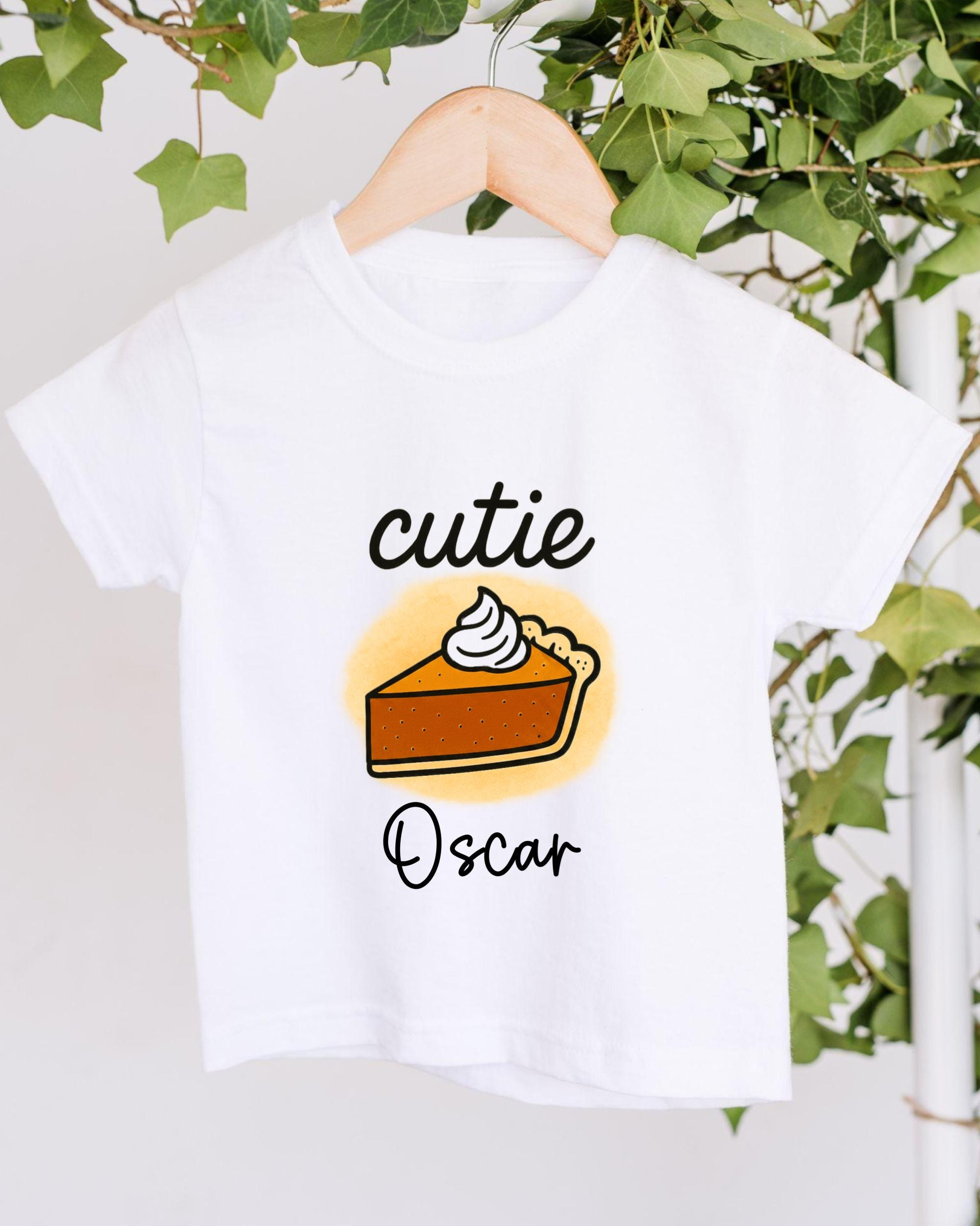 A white t-shirt with a graphic design of a slice of pie and the text "cutie Oscar" printed on it.