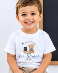A young boy wearing a white t-shirt with a teddy bear and a chalkboard, smiling at the camera.