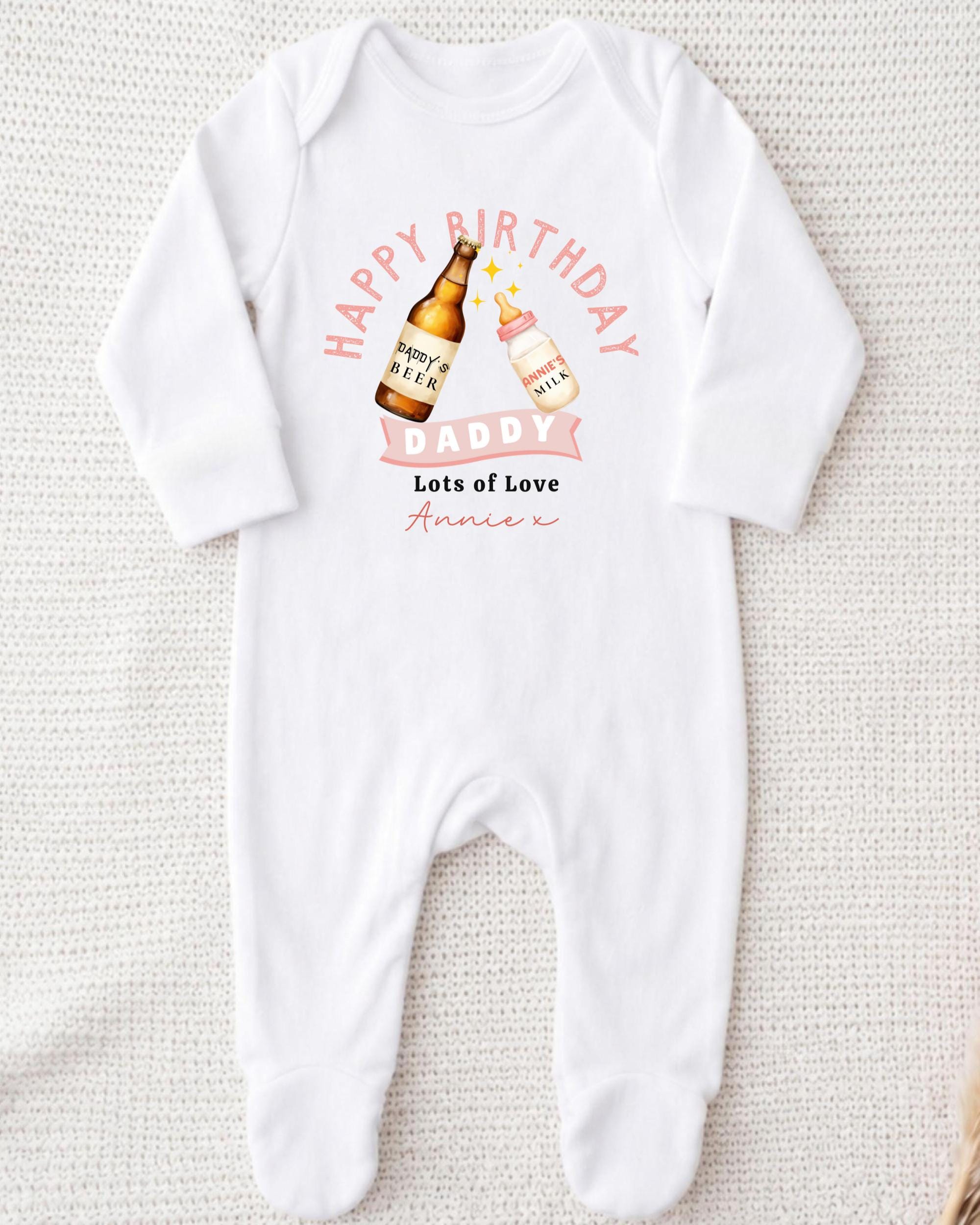 A white onesie with a graphic design on it, featuring a bottle of beer and a baby bottle, along with the text "Happy Birthday Daddy Lots of Love Annie" printed on it.