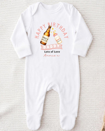 A white onesie with a graphic design on it, featuring a bottle of beer and a baby bottle, along with the text "Happy Birthday Daddy Lots of Love Annie" printed on it.