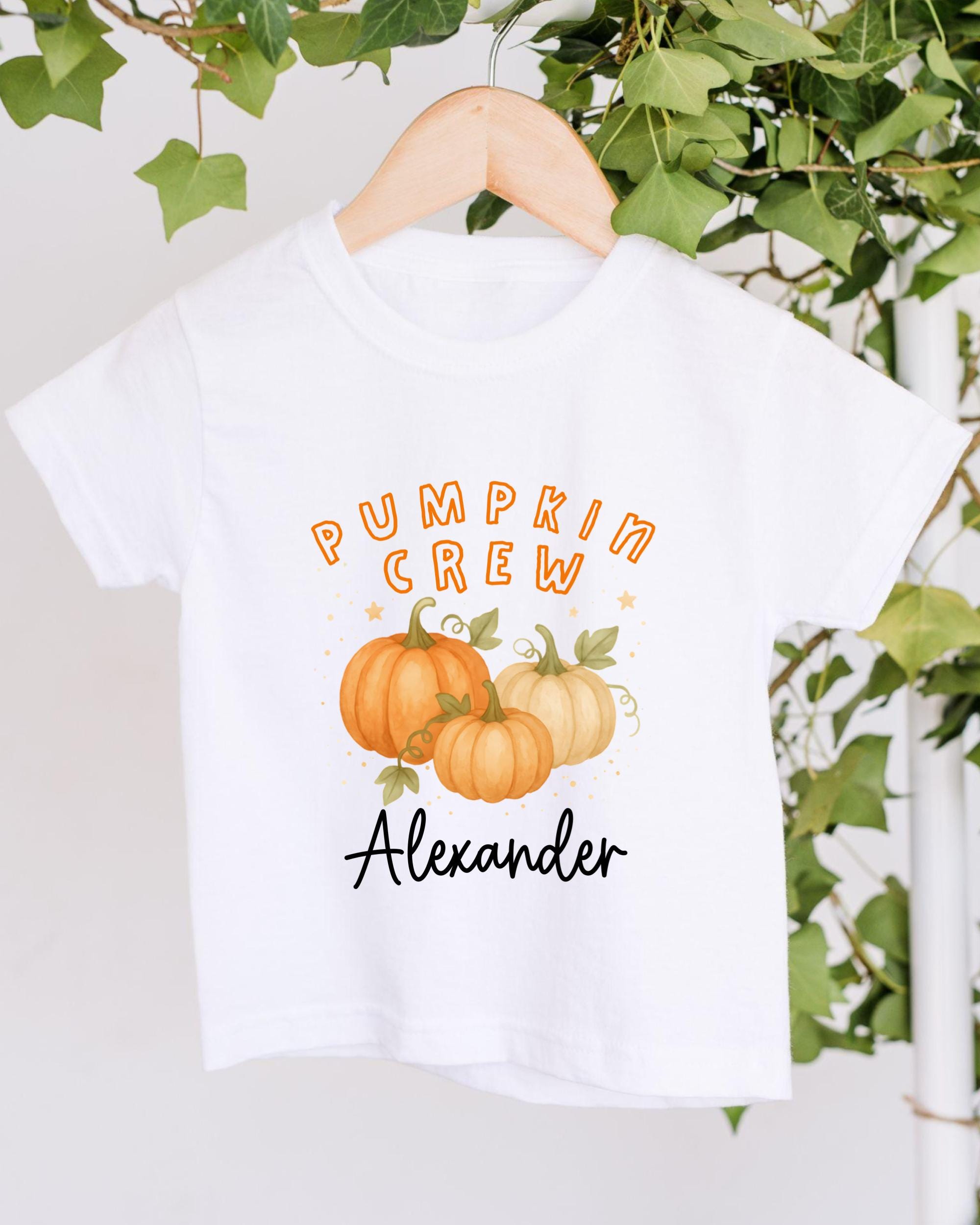 A white t-shirt with a graphic design featuring three pumpkins and the text "Pumpkin Crew Alexander" printed on it.