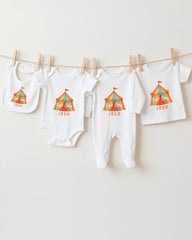 A collection of baby clothes, including onesies and bibs, hanging on a clothesline.