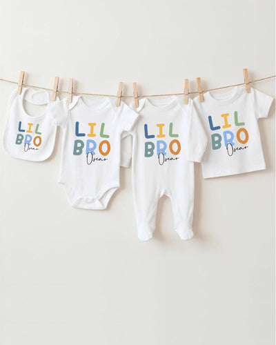 A row of four white baby clothes with the text "LIL BRO Oscar" printed on them, hanging on a clothesline.