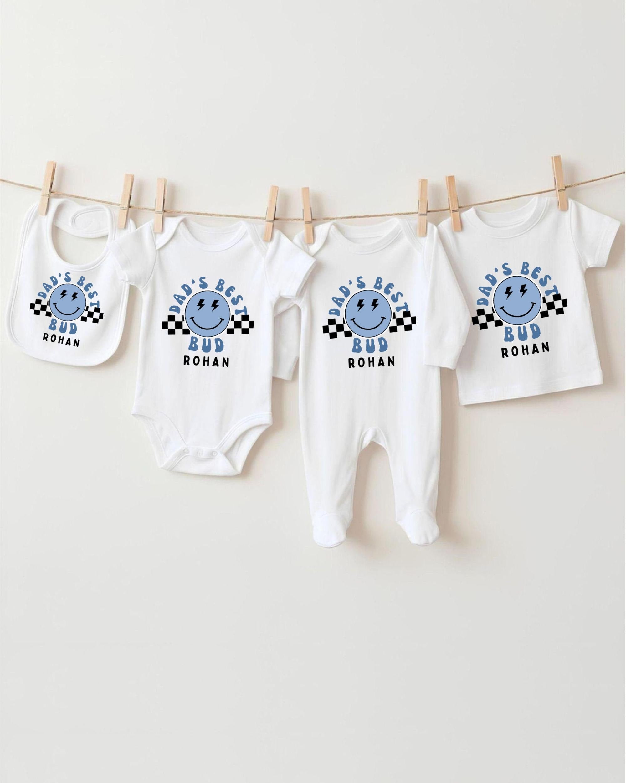 A collection of four white baby clothes, including onesies and bibs, hanging on a clothesline.
