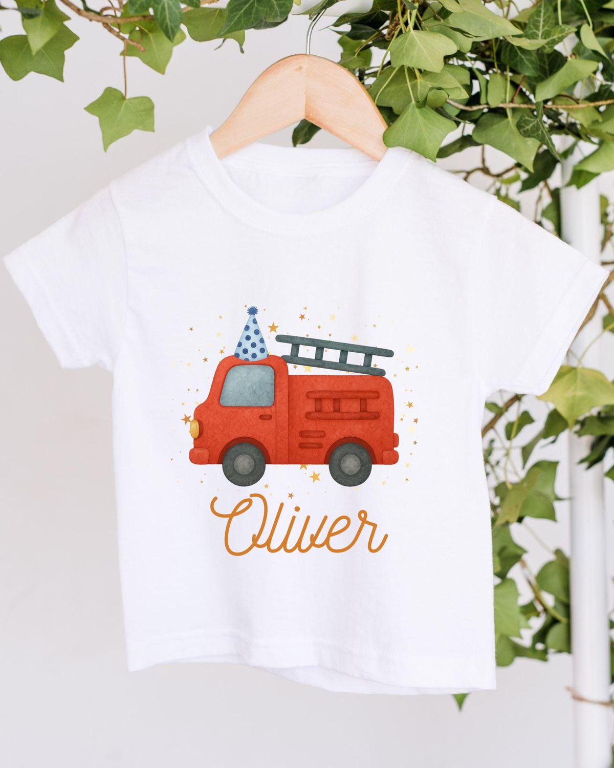 A white t-shirt with a red fire truck and a blue party hat printed on it, along with the name "Olivier" written below the image.