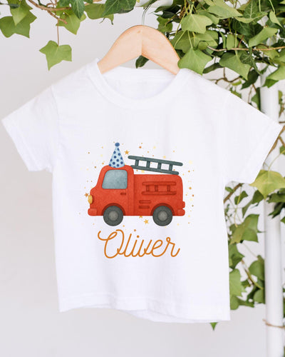 A white t-shirt with a red fire truck and a blue party hat printed on it, along with the name "Olivier" written below the image.