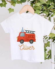 A white t-shirt with a red fire truck and a blue party hat printed on it, along with the name "Olivier" written below the image.