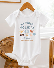 A white baby onesie with a printed design and text on it, hanging on a wooden hanger.
