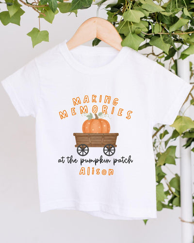 A white t-shirt with a graphic design featuring a pumpkin and a wagon, along with the text "Making memories at the pumpkin patch Alison".