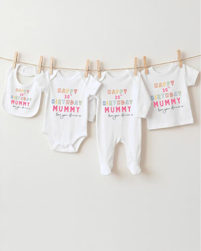 A row of four white baby clothes, including onesies and bibs, hanging on a clothesline.