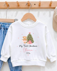 A white sweater with a Christmas tree and a teddy bear printed on it, along with the text "My first Christmas Olivia 2020".