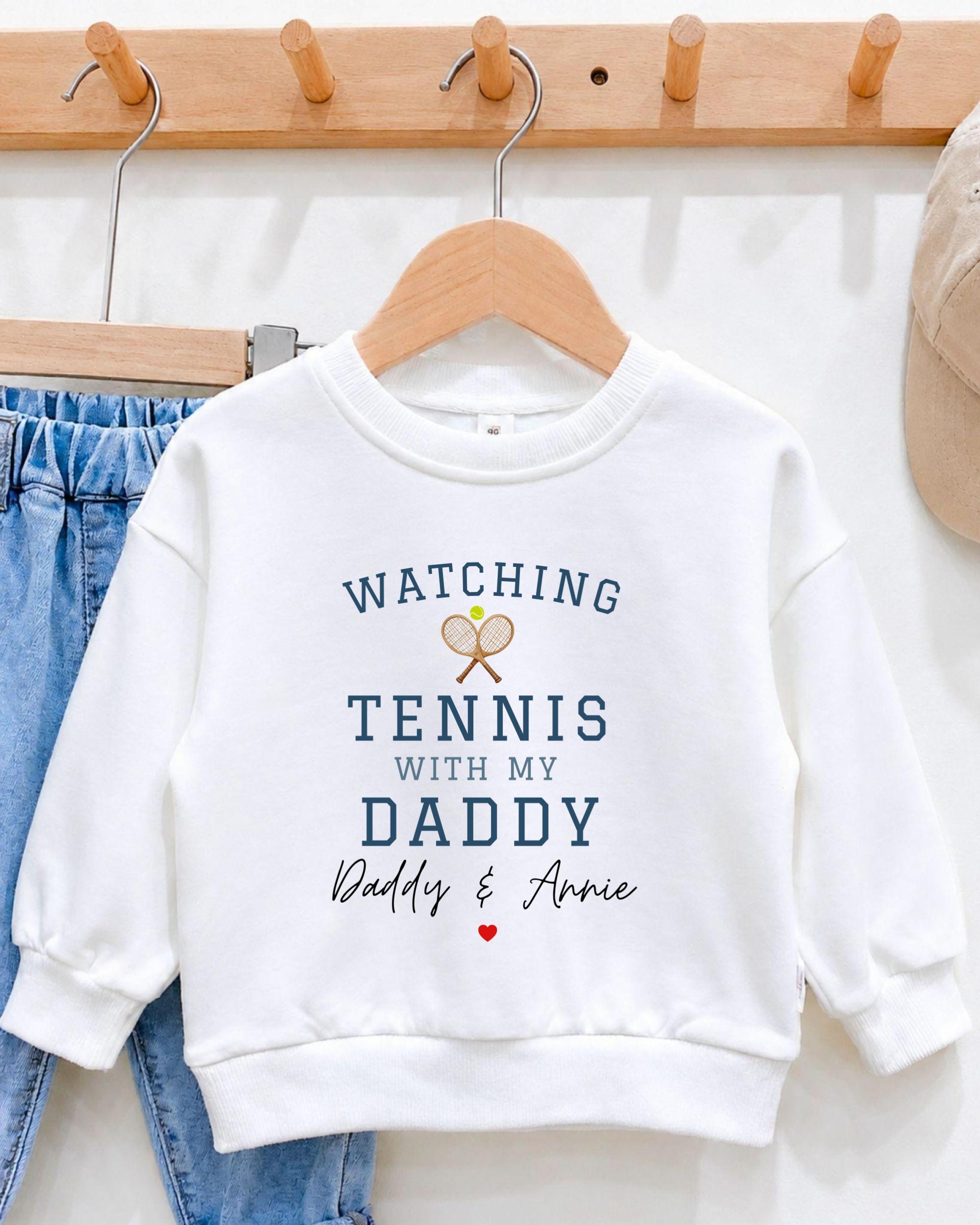 A white sweatshirt with the text "WATCHING TENNIS WITH MY DADY Daddy & Annie" printed on it, along with tennis rackets and a heart symbol.