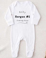 A white onesie with text printed on it, indicating that the baby is expected to arrive soon.