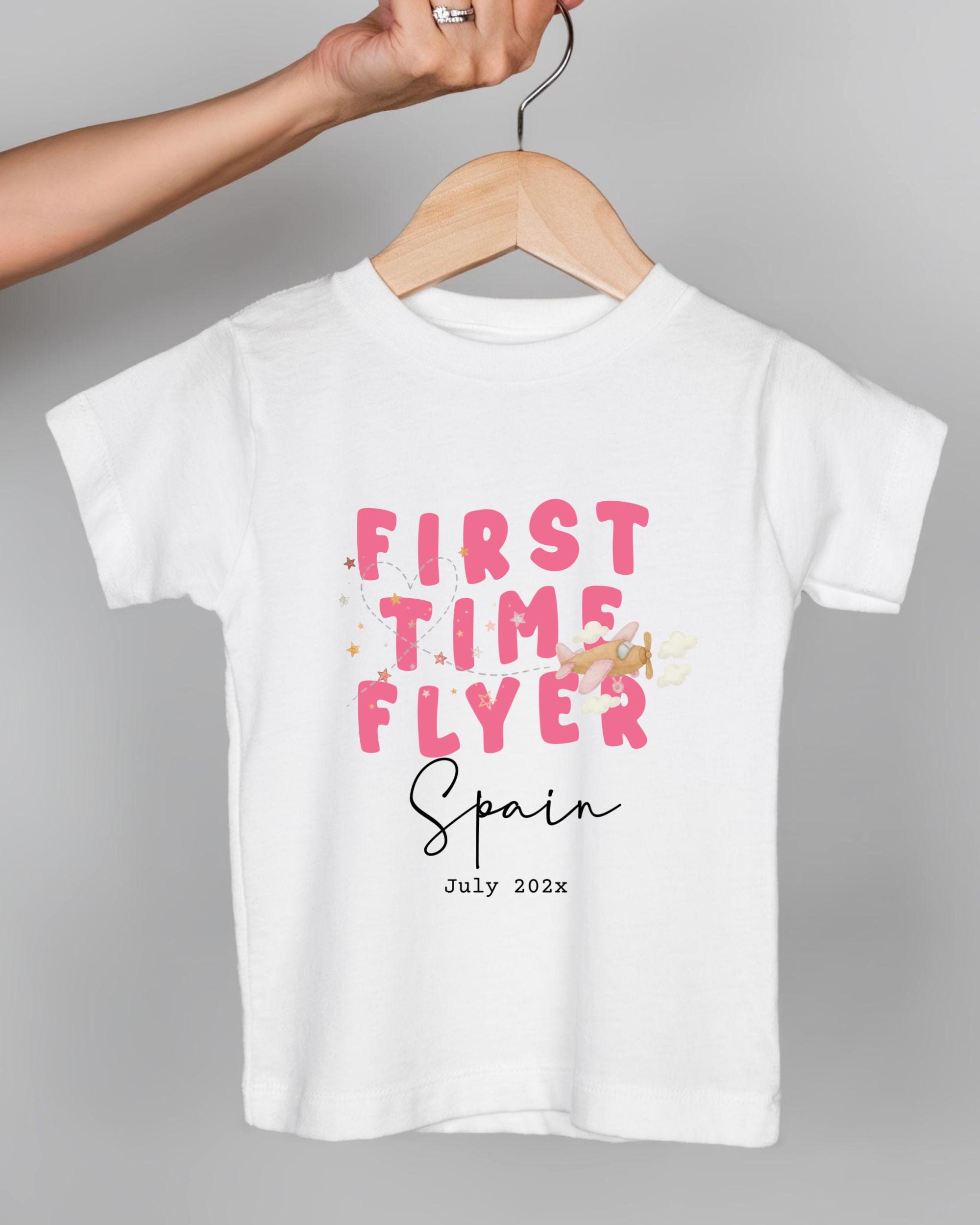 A white t-shirt with pink text and a graphic design, hanging on a wooden hanger.